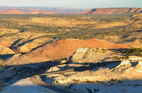 A scenic view of rugged, colorful desert terrain with a winding road cutting through the landscape.