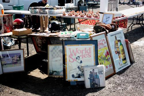 A table at a flea market displaying various vintage items, including posters, shoes, and collectibles.