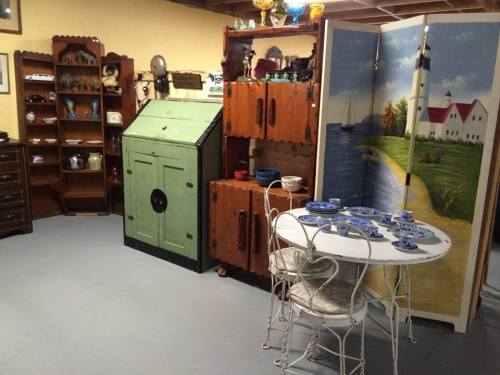 A cozy vintage room featuring a green cabinet, wooden shelves, and a small dining table set with blue dishes.
