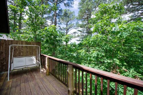 A wooden deck surrounded by lush green trees under a bright blue sky, featuring a swing seat.