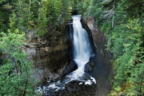 A serene waterfall cascading down rocky cliffs, surrounded by lush green trees and a tranquil forest setting.