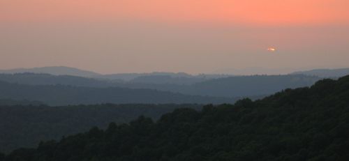 A serene sunset over rolling hills, with soft orange hues blending into the evening sky.