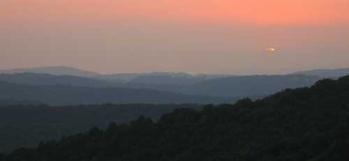 A serene sunset over rolling hills, with soft orange hues blending into the evening sky.