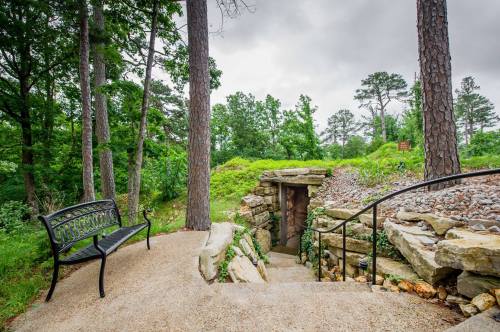 A stone entrance leads down a path surrounded by greenery, with a bench nearby under a cloudy sky.