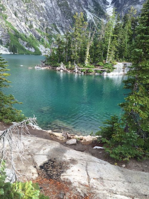 A serene lake surrounded by lush green trees and rocky shores, reflecting the mountains in the background.