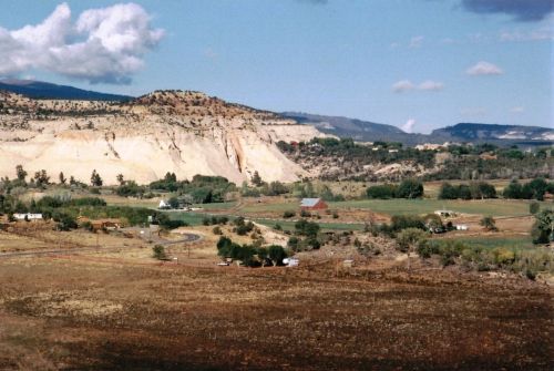 A scenic landscape featuring rolling hills, a farm, and distant mountains under a partly cloudy sky.