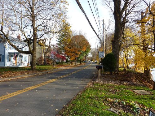 A quiet suburban street lined with trees, houses, and autumn foliage, featuring a speed limit sign of 25 mph.