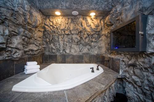 A luxurious bathroom featuring a stone wall, a white jacuzzi tub, and neatly stacked towels on the edge.