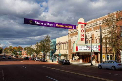 Main street view of Albion College with a "Homecoming" banner and historic buildings under a cloudy sky.