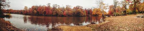 A serene river scene surrounded by vibrant autumn foliage and a sandy shore, reflecting the colorful trees.