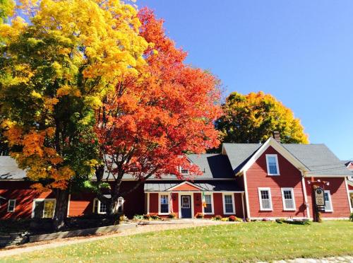 A red house surrounded by vibrant autumn trees with yellow and orange leaves under a clear blue sky.