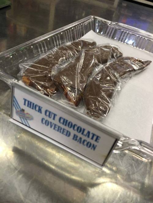 A clear container holding several pieces of thick cut chocolate-covered bacon, labeled for sale.