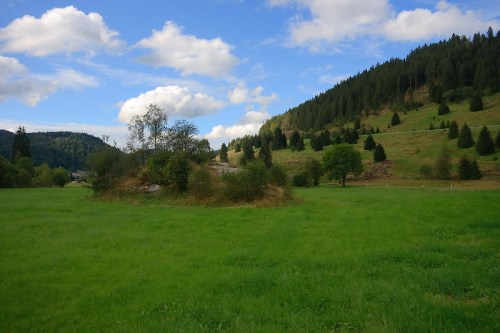 A lush green field surrounded by hills and trees under a partly cloudy sky.