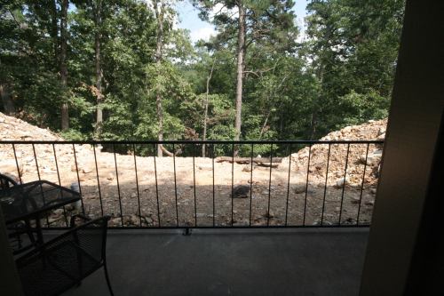 View from a balcony overlooking a wooded area with trees and a cleared patch of land.