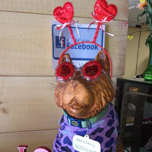 A dog statue wearing heart-shaped glasses and antennae with hearts, dressed in a purple shirt, welcomes visitors.