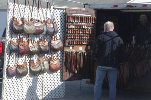 A person browsing a market stall displaying leather bags and belts.