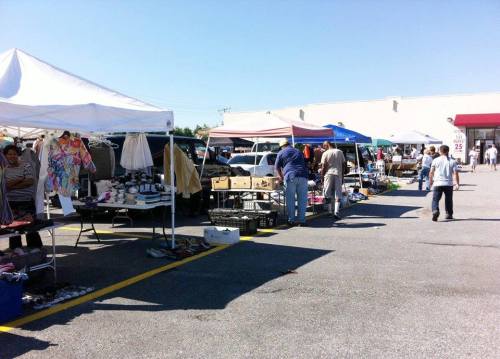 A bustling outdoor market with various tents and vendors selling goods under a clear blue sky.