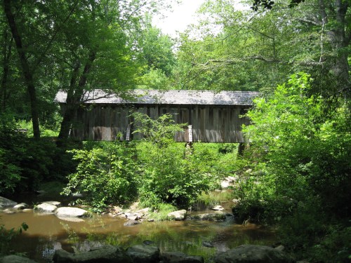 A rustic wooden covered bridge surrounded by lush greenery and a small stream.
