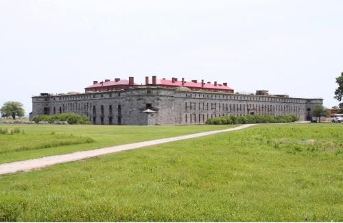 Historic stone building with a red roof, surrounded by green grass and a dirt path leading to it.