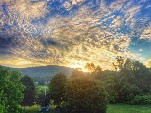 A vibrant sunset over rolling hills, with colorful clouds and lush green trees in the foreground.