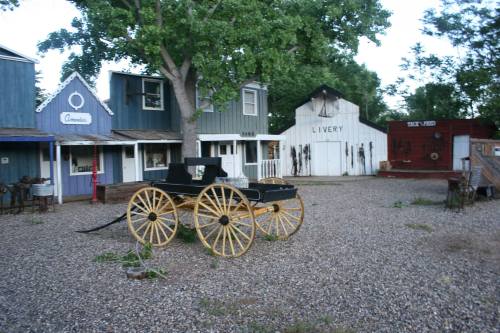 A historic western town scene featuring a horse-drawn carriage and colorful wooden buildings in a gravel area.