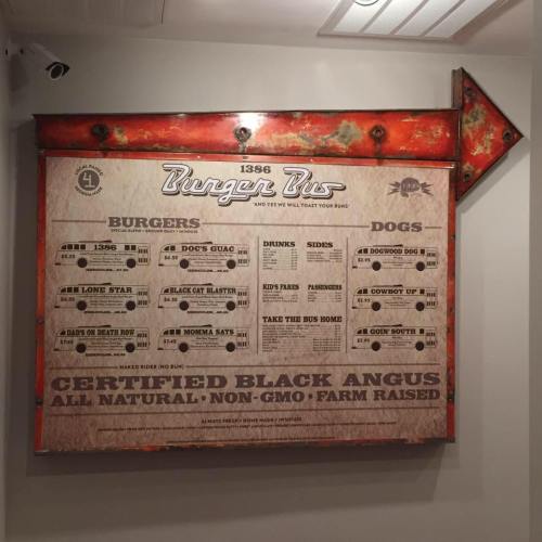 Menu board for Burger Pit featuring burgers, hot dogs, drinks, and farm-raised ingredients, with an arrow pointing right.