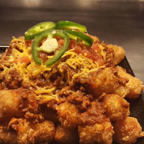 A plate of loaded tater tots topped with chili, cheese, jalapeños, and diced tomatoes.