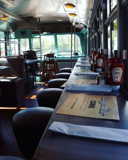 Interior of a converted bus with a long counter, stools, and condiments like ketchup on the tables.