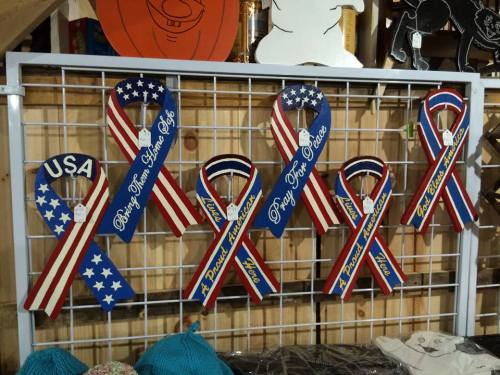 A display of wooden patriotic ribbons in red, white, and blue, featuring phrases like "USA" and "Proud American."