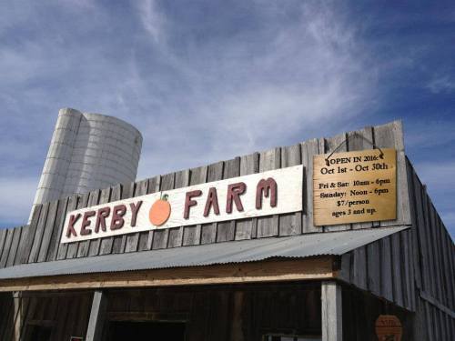Sign for Kerby Farm with hours of operation, featuring a rustic wooden structure and a silo in the background.