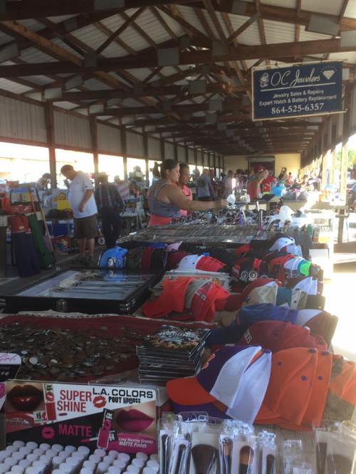 A bustling market scene with tables displaying various merchandise, including hats, jewelry, and cosmetics.