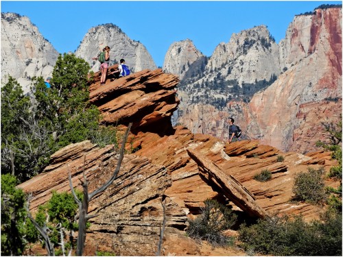A group of hikers on a rocky outcrop with towering mountains in the background under a clear blue sky.