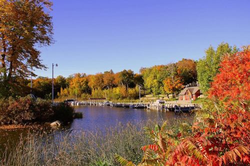A serene river scene with colorful autumn foliage, docks, and a cozy cabin under a clear blue sky.