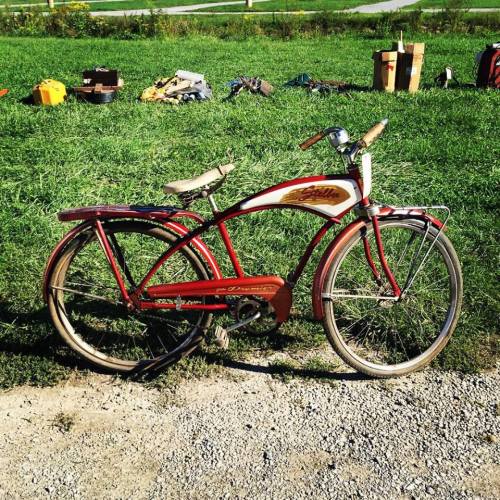 A vintage red bicycle with a decorative design, resting on a gravel path beside green grass.