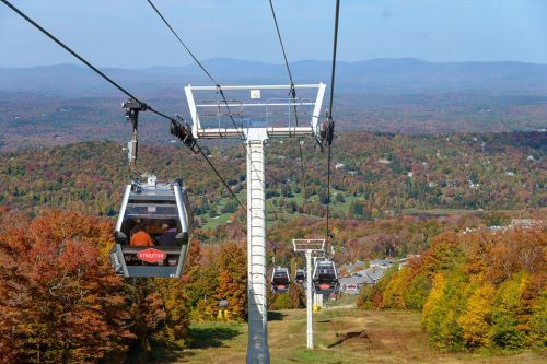 A scenic view of a ski lift with gondolas, surrounded by colorful autumn foliage and distant mountains.
