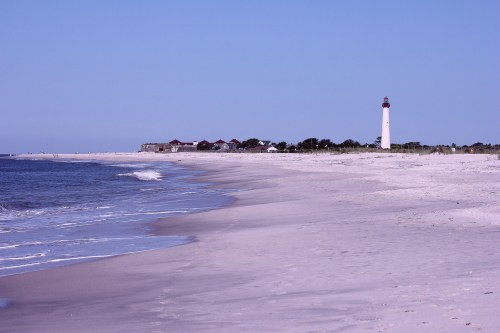 A serene beach scene with gentle waves, a lighthouse in the distance, and a clear blue sky.