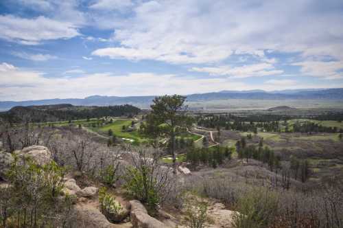 A scenic landscape featuring rolling hills, green fields, and a blue sky with clouds, framed by rocky terrain.