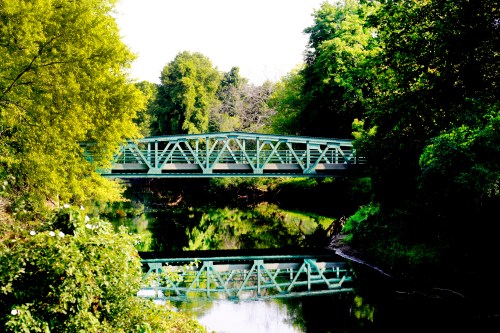 A green bridge spans a calm river, surrounded by lush trees and reflecting in the water below.