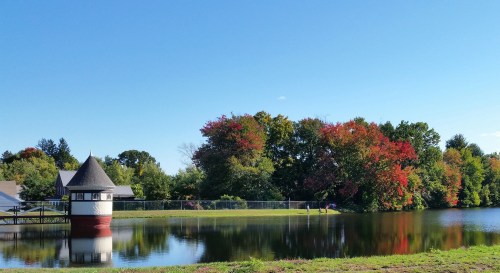 A serene lake scene with a gazebo, colorful autumn trees, and a clear blue sky reflecting on the water.