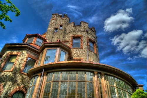 A stone castle with a turret, featuring large windows and a dramatic sky with clouds.