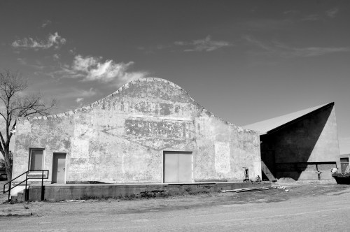 A black and white image of two unique, weathered buildings with distinct architectural shapes against a cloudy sky.