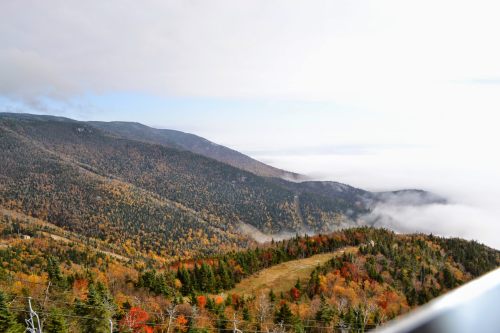 A scenic view of mountains covered in autumn foliage, with clouds rolling over the valleys below.