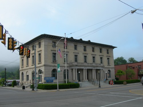 Historic building with columns, flags, and traffic lights at a street intersection, surrounded by greenery and fog.