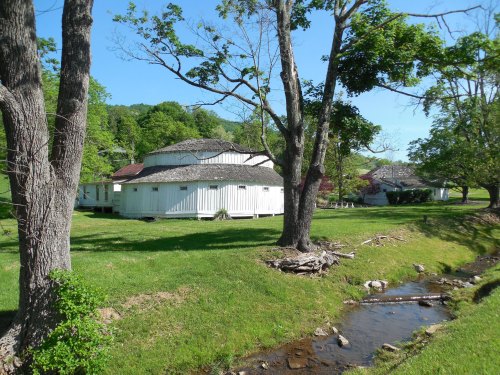 A circular white building surrounded by trees and green grass, with a small stream flowing nearby.