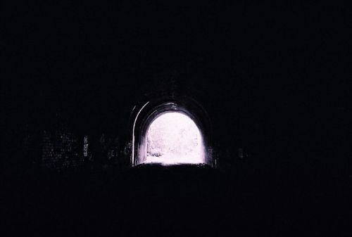 A dark tunnel with a bright light at the end, creating a contrast between shadow and illumination.