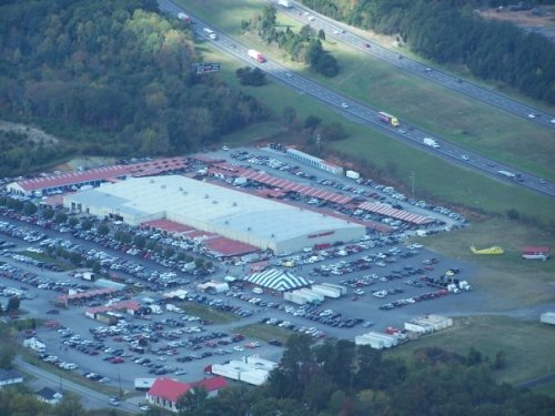 Aerial view of a large retail store with a parking lot filled with cars, near a highway and surrounded by trees.