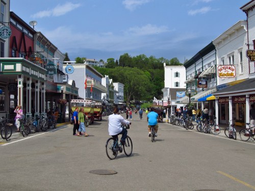 A bustling street scene with people biking and walking among shops and restaurants on a sunny day.
