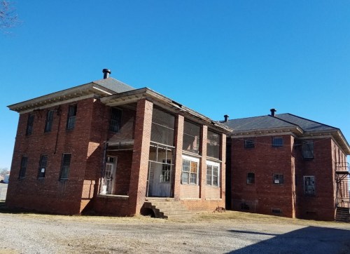 Abandoned two-story brick building with a screened porch and a clear blue sky in the background.