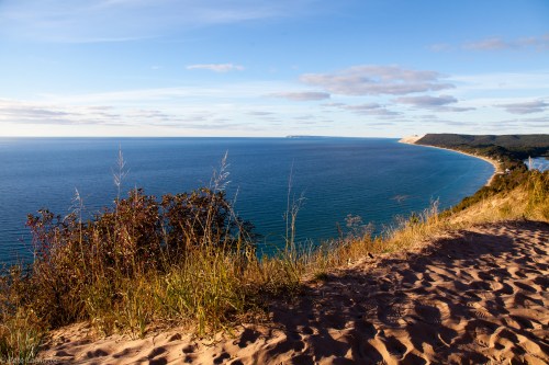 A scenic view of a coastline with sandy hills, blue water, and a clear sky, capturing the beauty of nature.