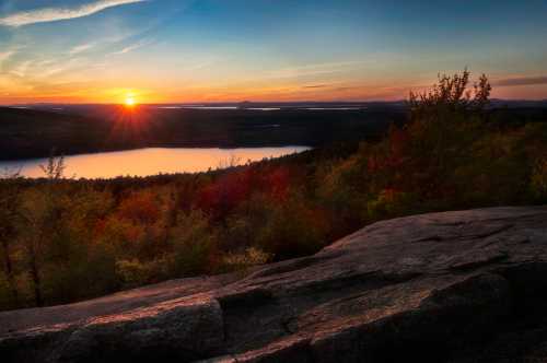 A vibrant sunset over a tranquil lake, surrounded by colorful trees and rocky terrain.